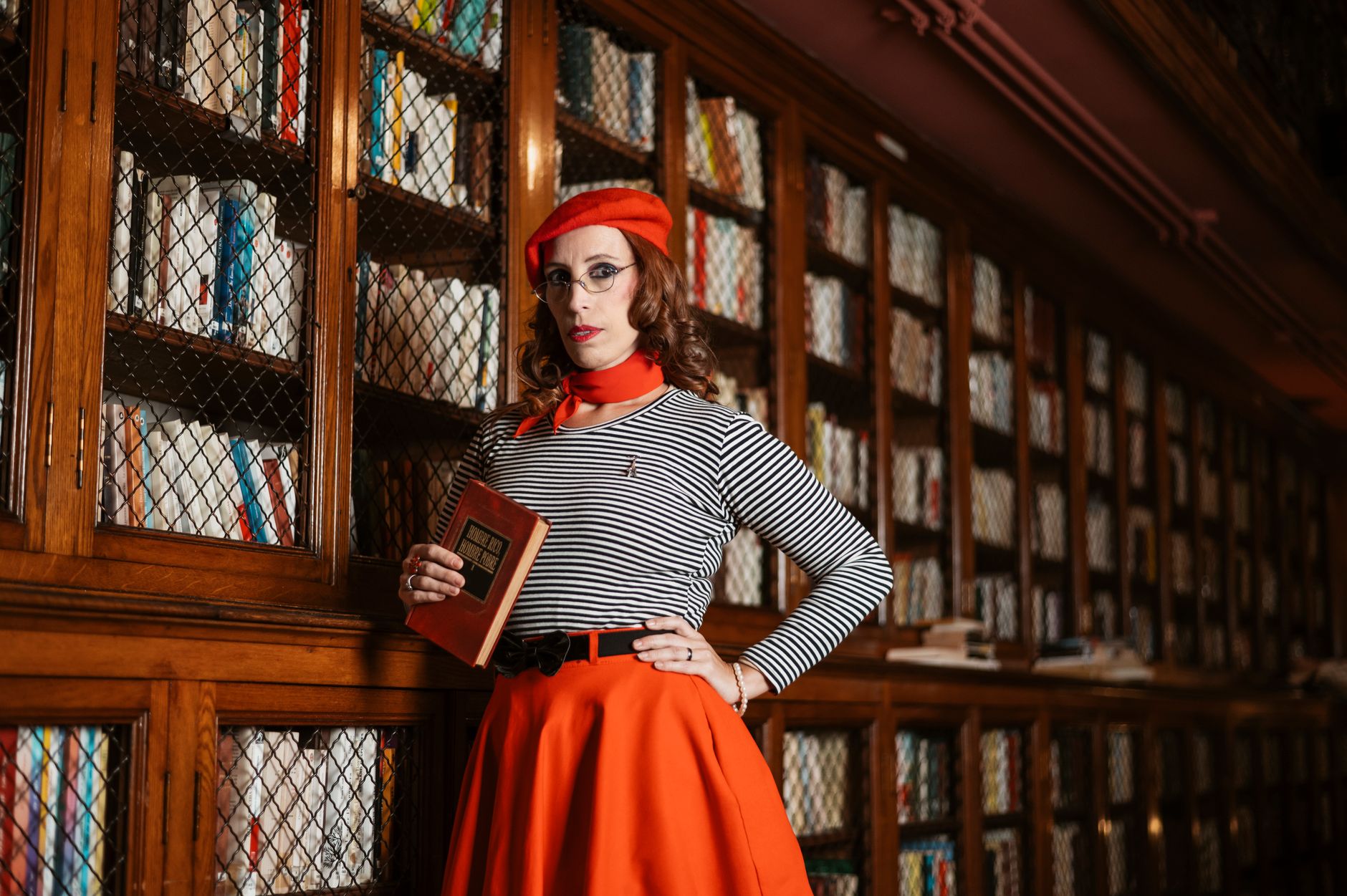 Fashionable woman with red beret and dress poses in an elegant library, Argentina.