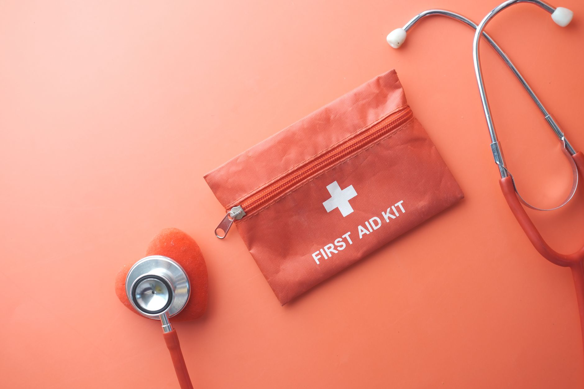 Medical tools including a stethoscope and first aid kit on a pink surface, perfect for healthcare themes.