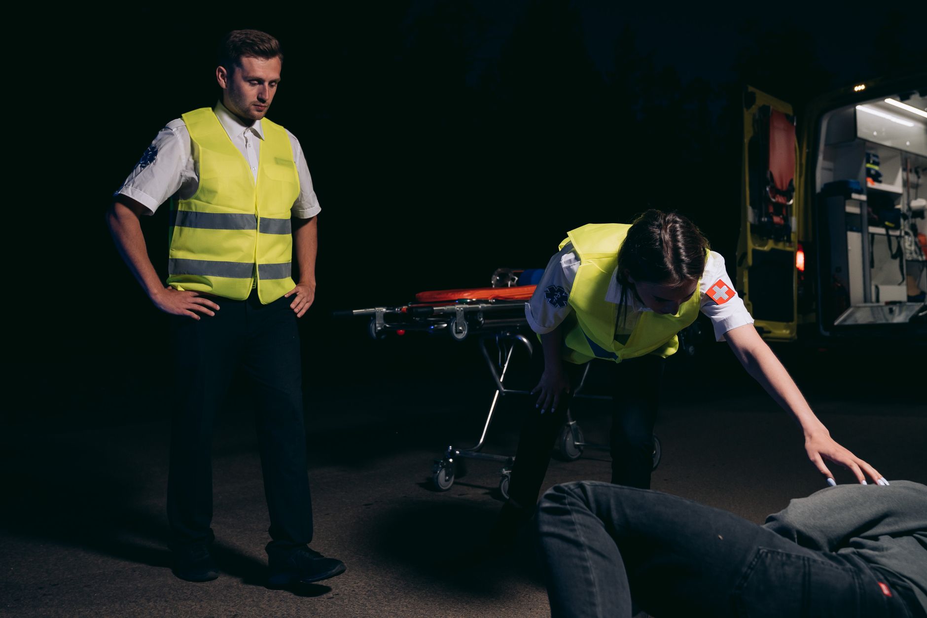 Emergency medical team attending to a patient at night with an ambulance in the background.