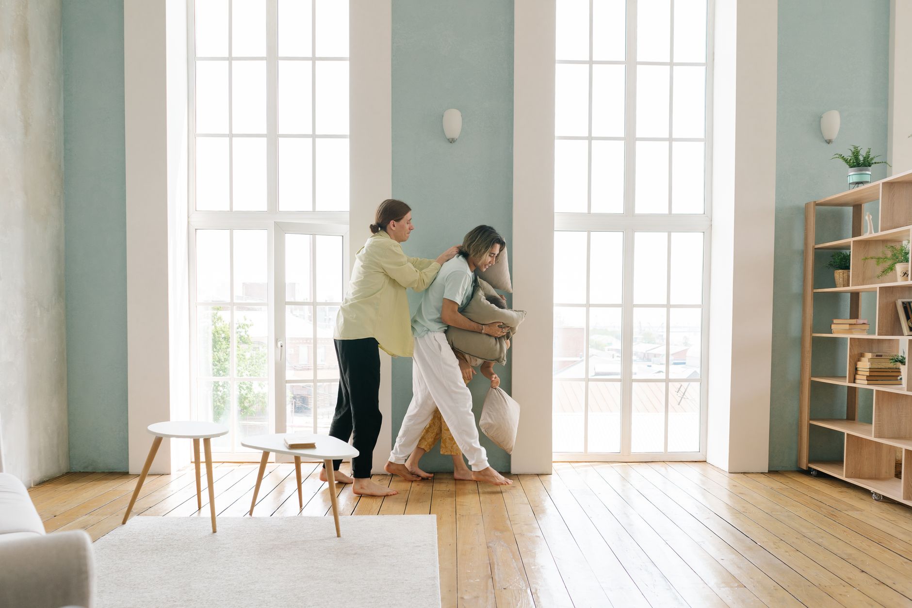Two people enjoying a playful pillow fight in a cozy and bright living room setting.