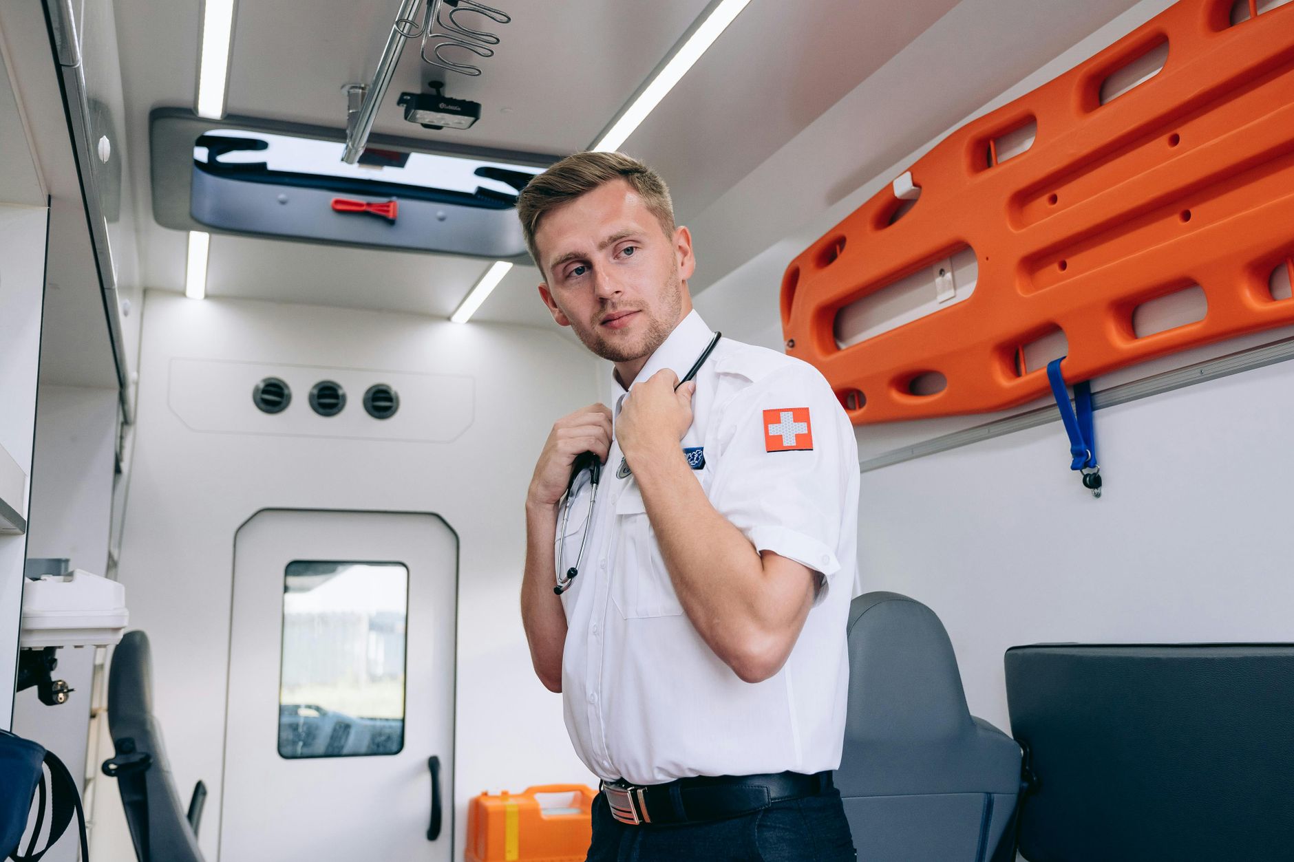 Paramedic standing inside the ambulance van, holding a stethoscope, ready for emergency response.
