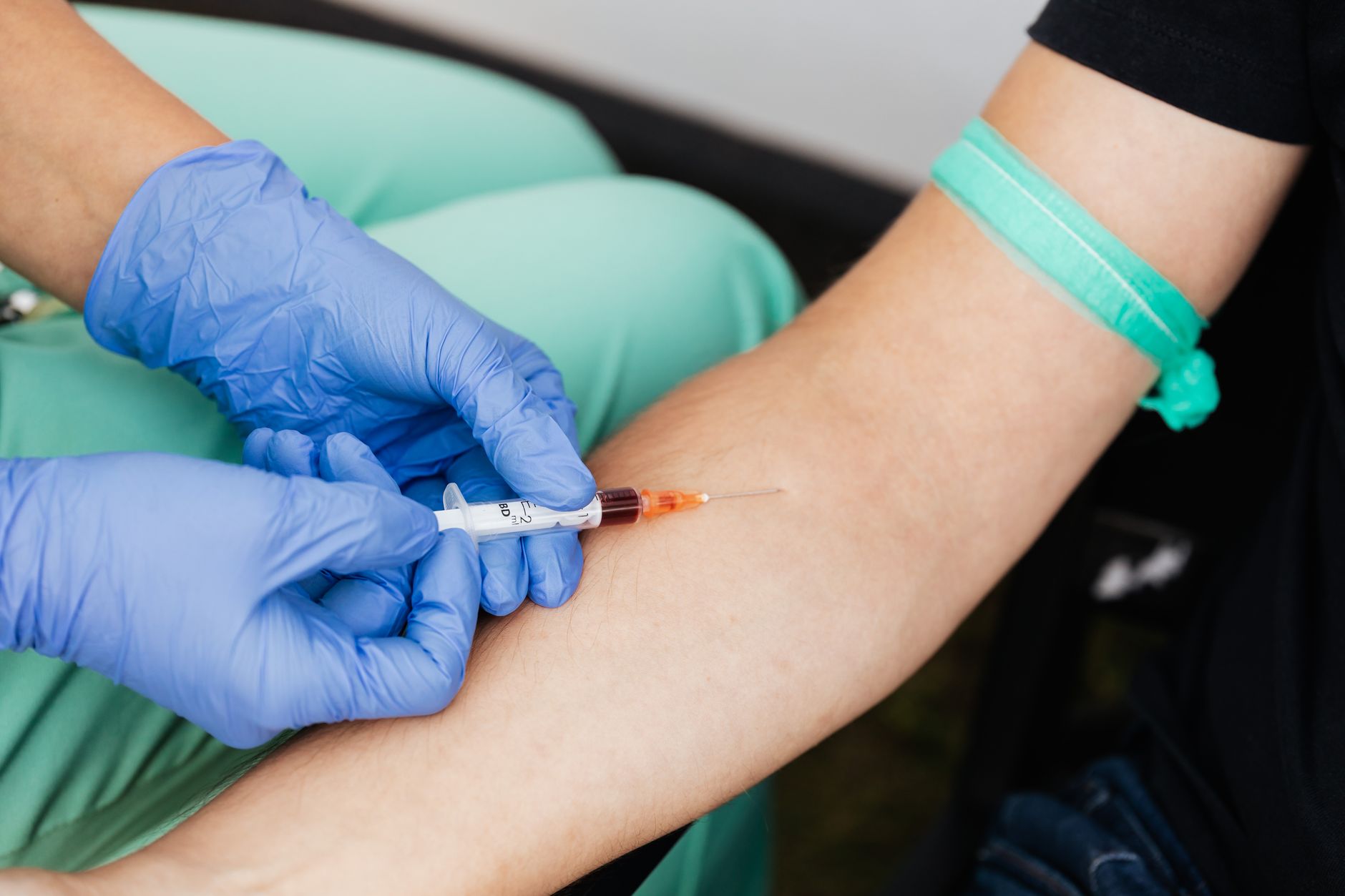 Healthcare worker drawing blood from patient's arm with syringe.