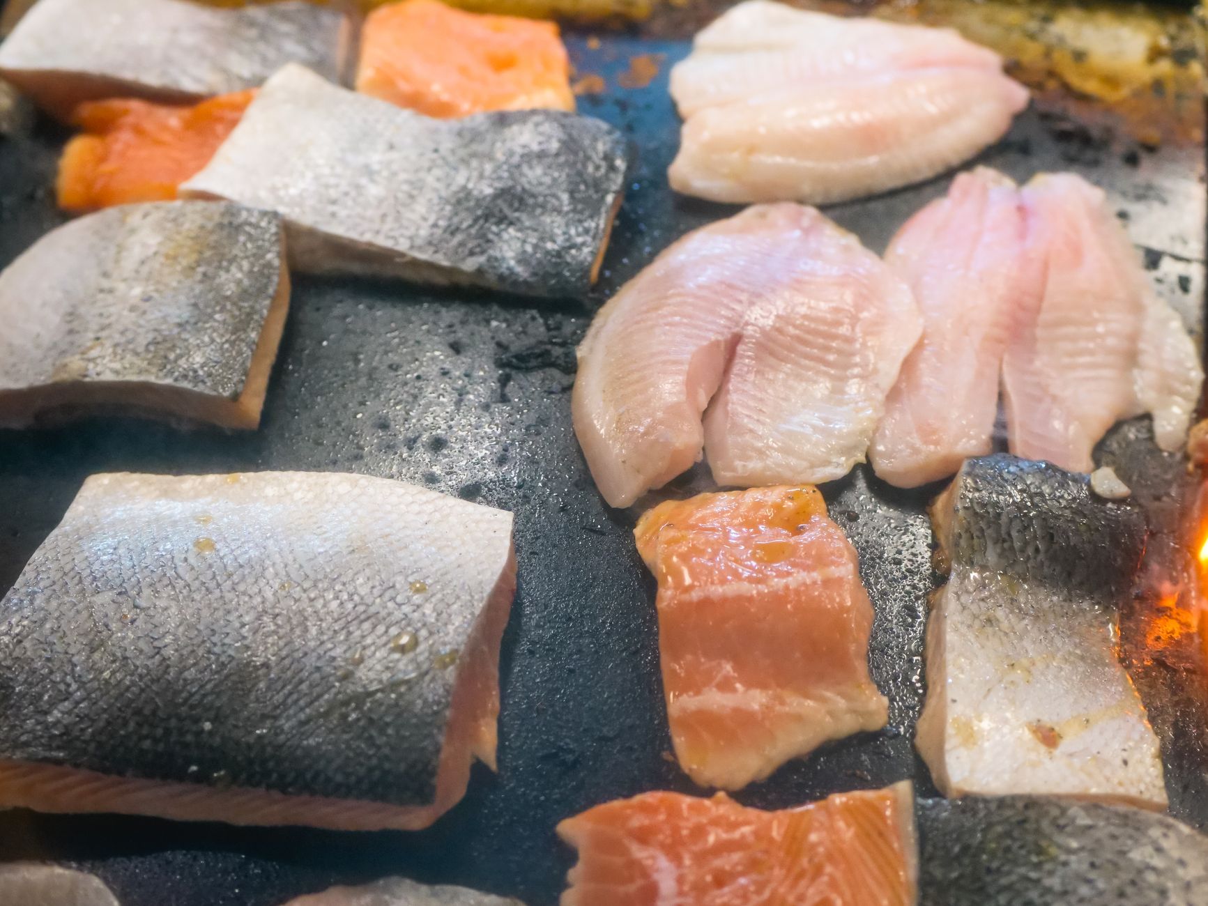 Top view of raw assorted fish fillets on a griddle, perfect for food enthusiasts.