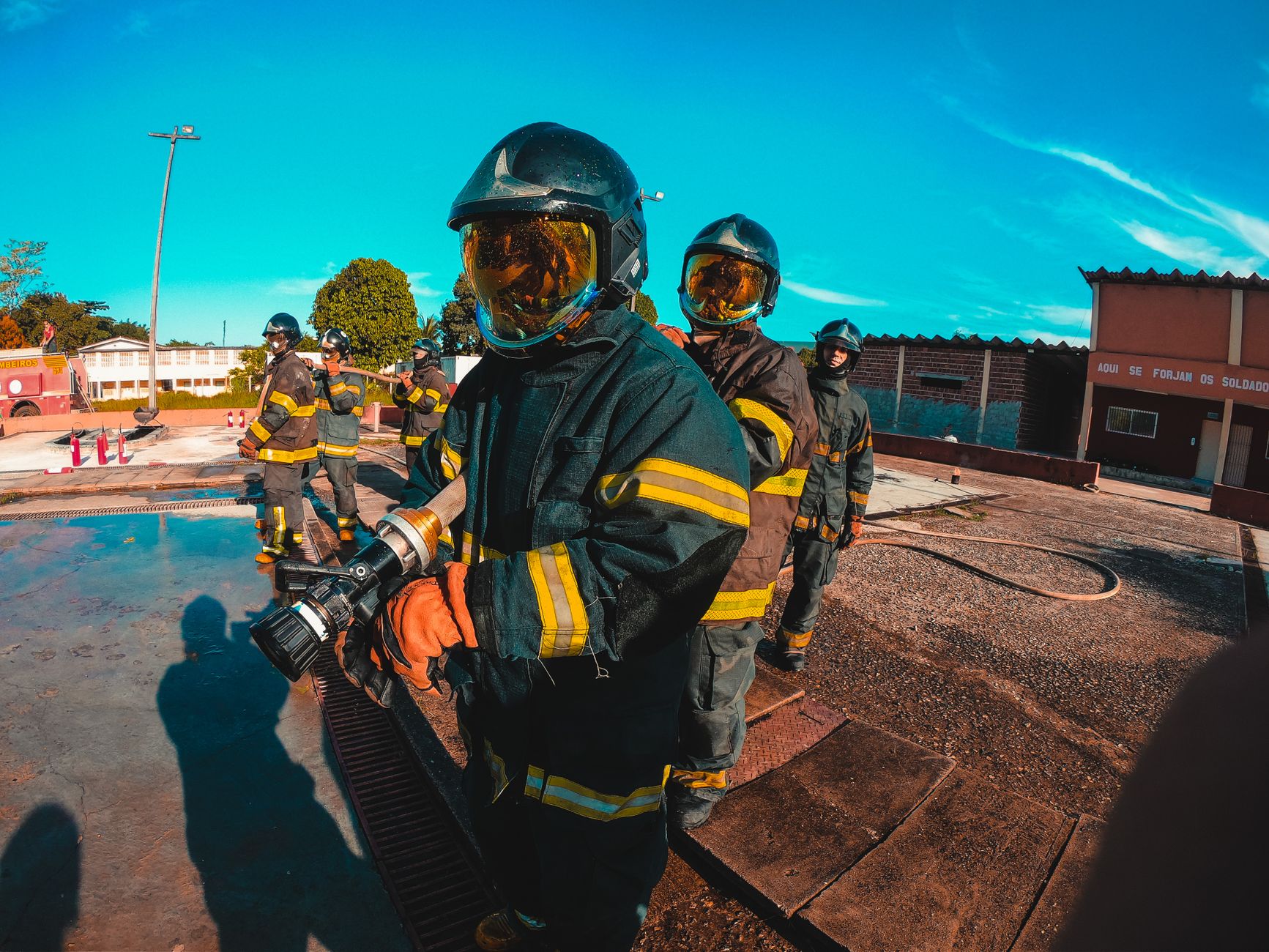 Firefighters in protective suits and helmets manage equipment during training outdoors.