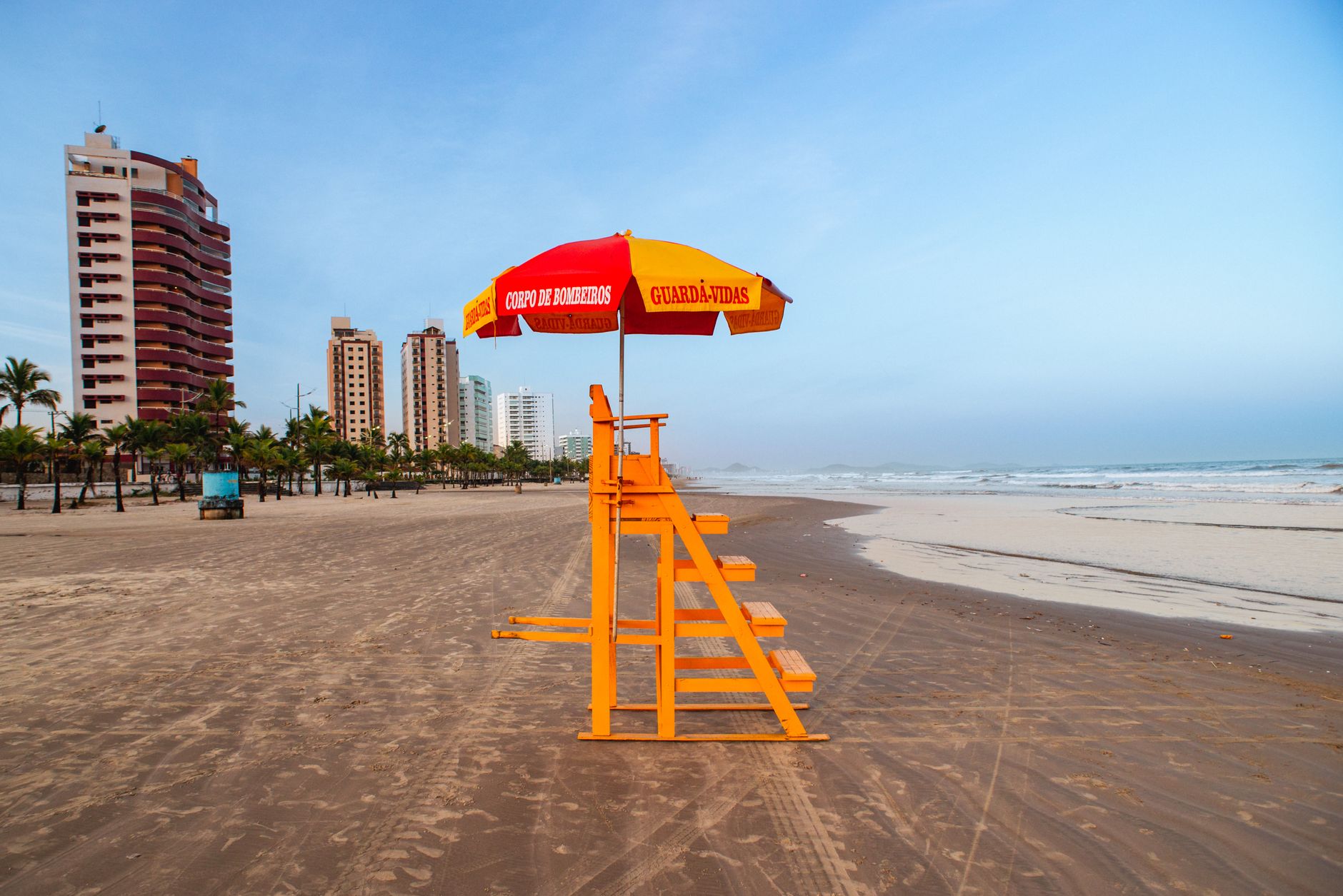 Bright lifeguard tower and umbrella on a tropical beach with city skyline.