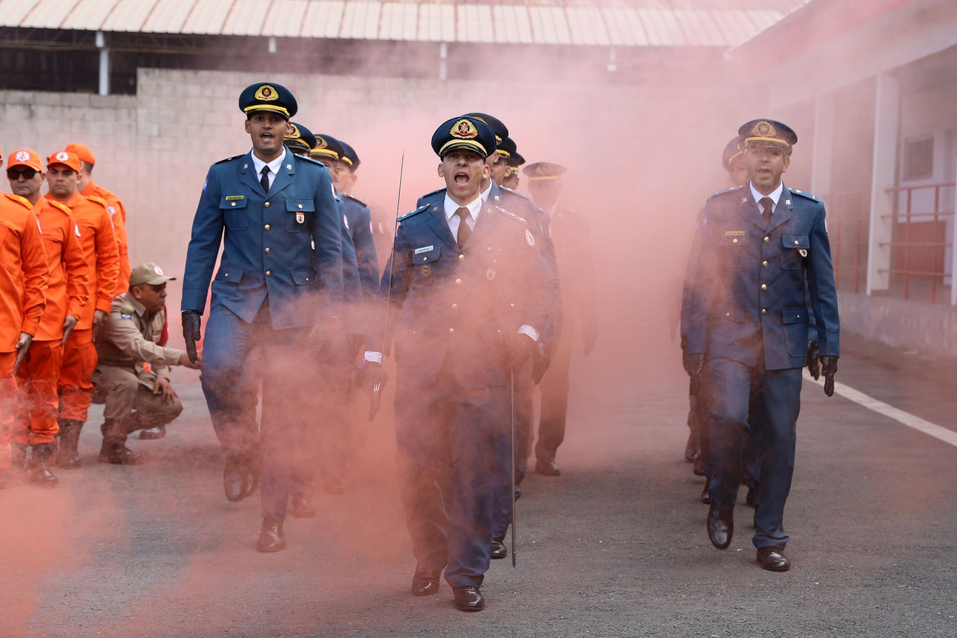 Military officers and firefighters participating in a ceremonial parade in Mato Grosso, Brazil, with smoke effects.