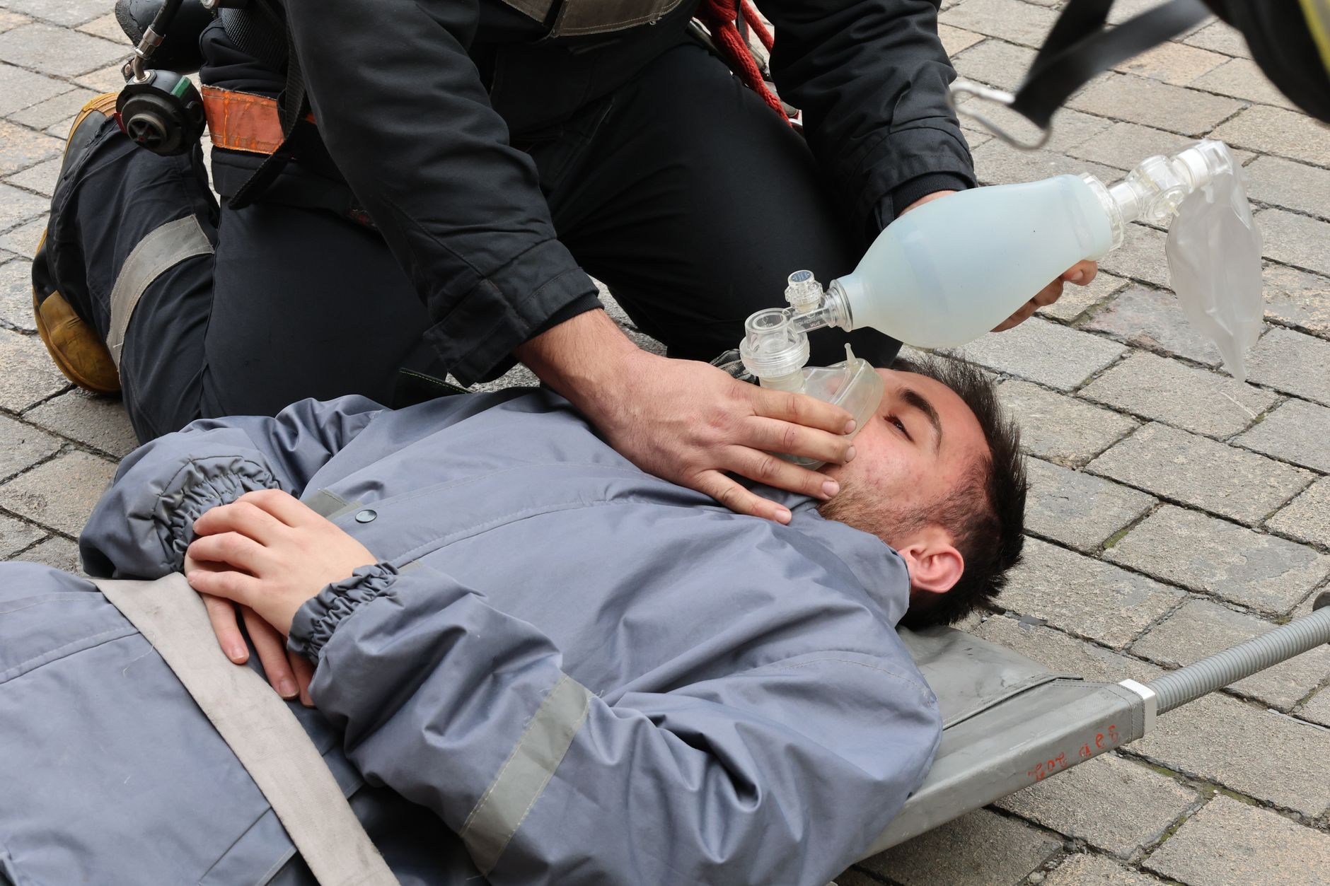 Firefighter providing oxygen mask to injured person during rescue operation outdoors.