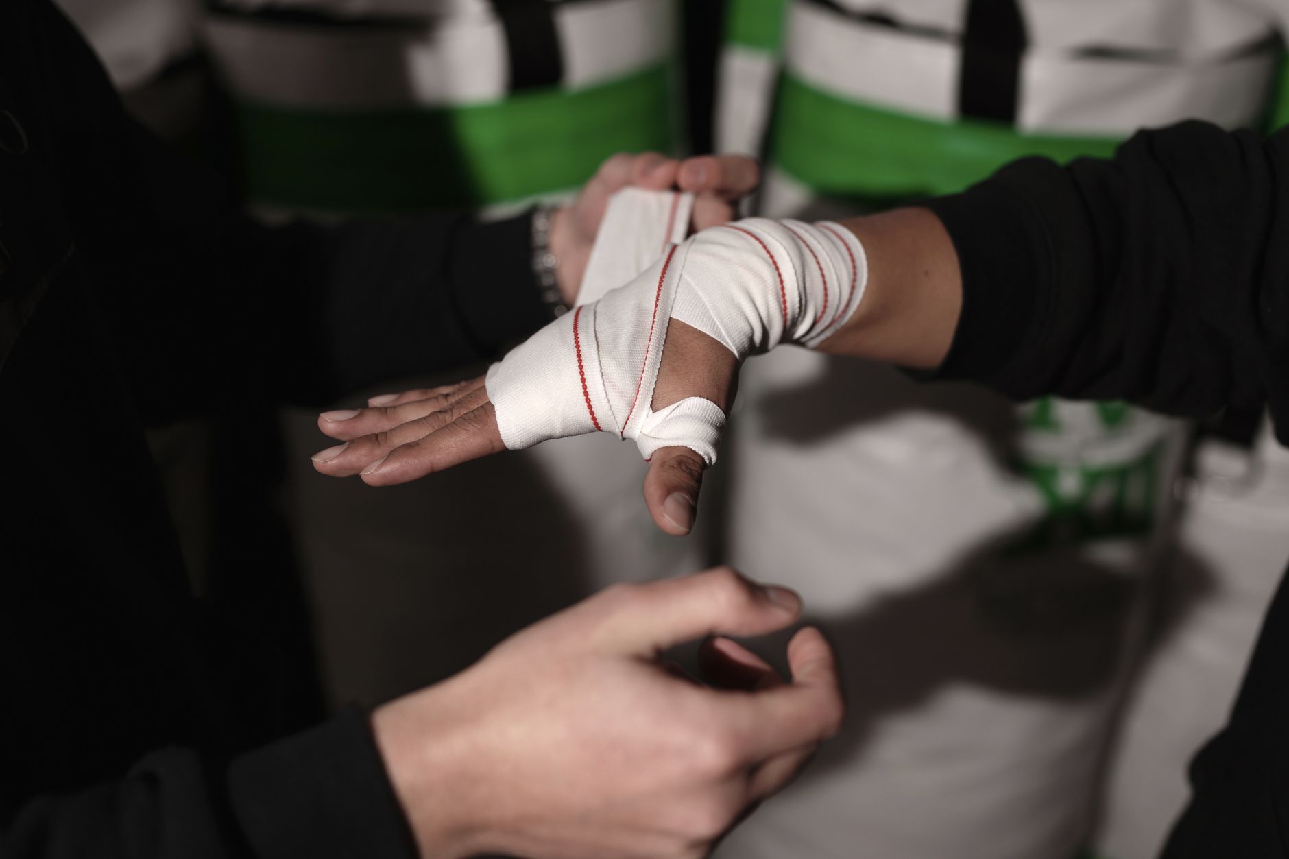 Close-up of a trainer wrapping a boxer's hand with white bandages indoors.