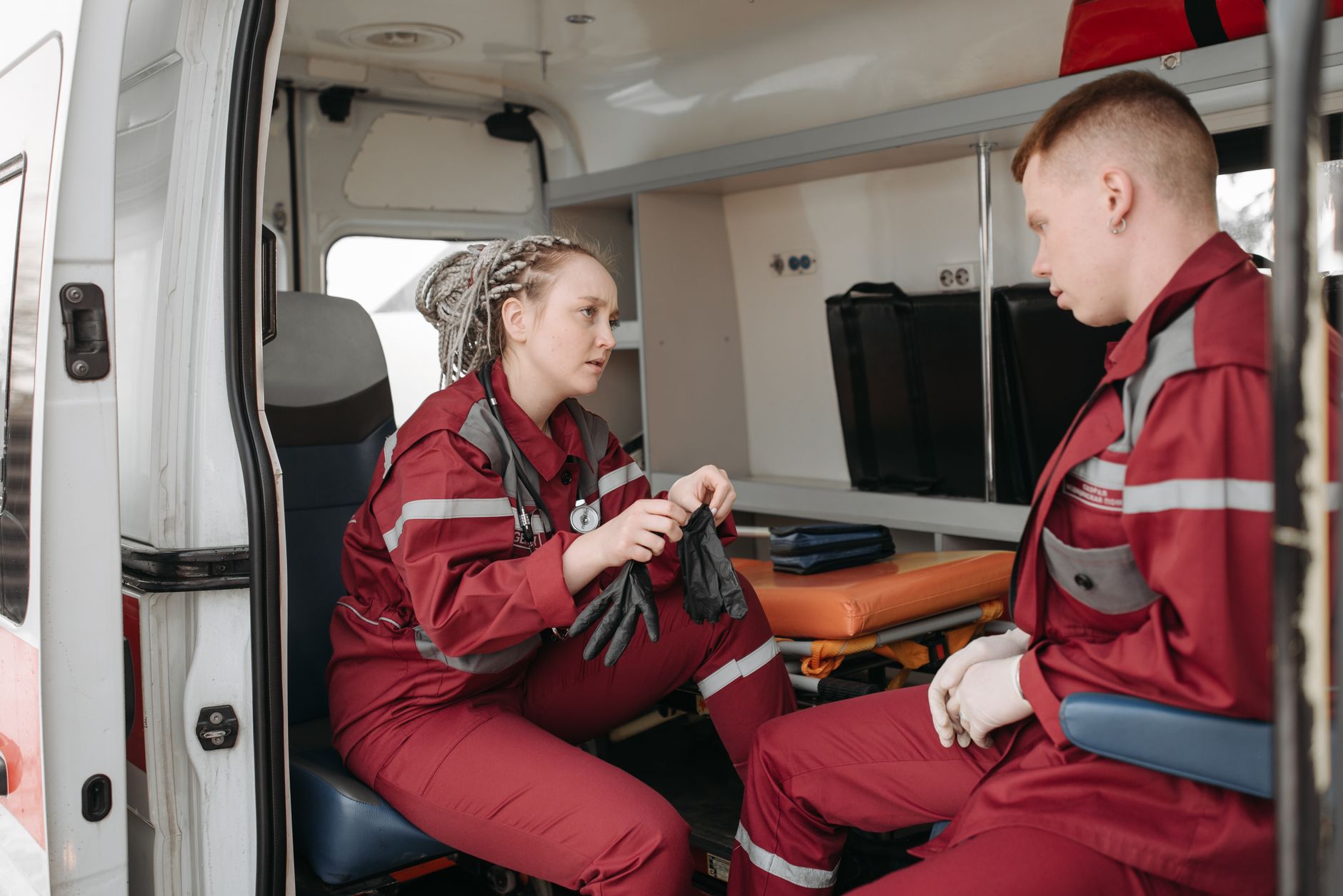 Two paramedics in uniform preparing equipment inside an ambulance.