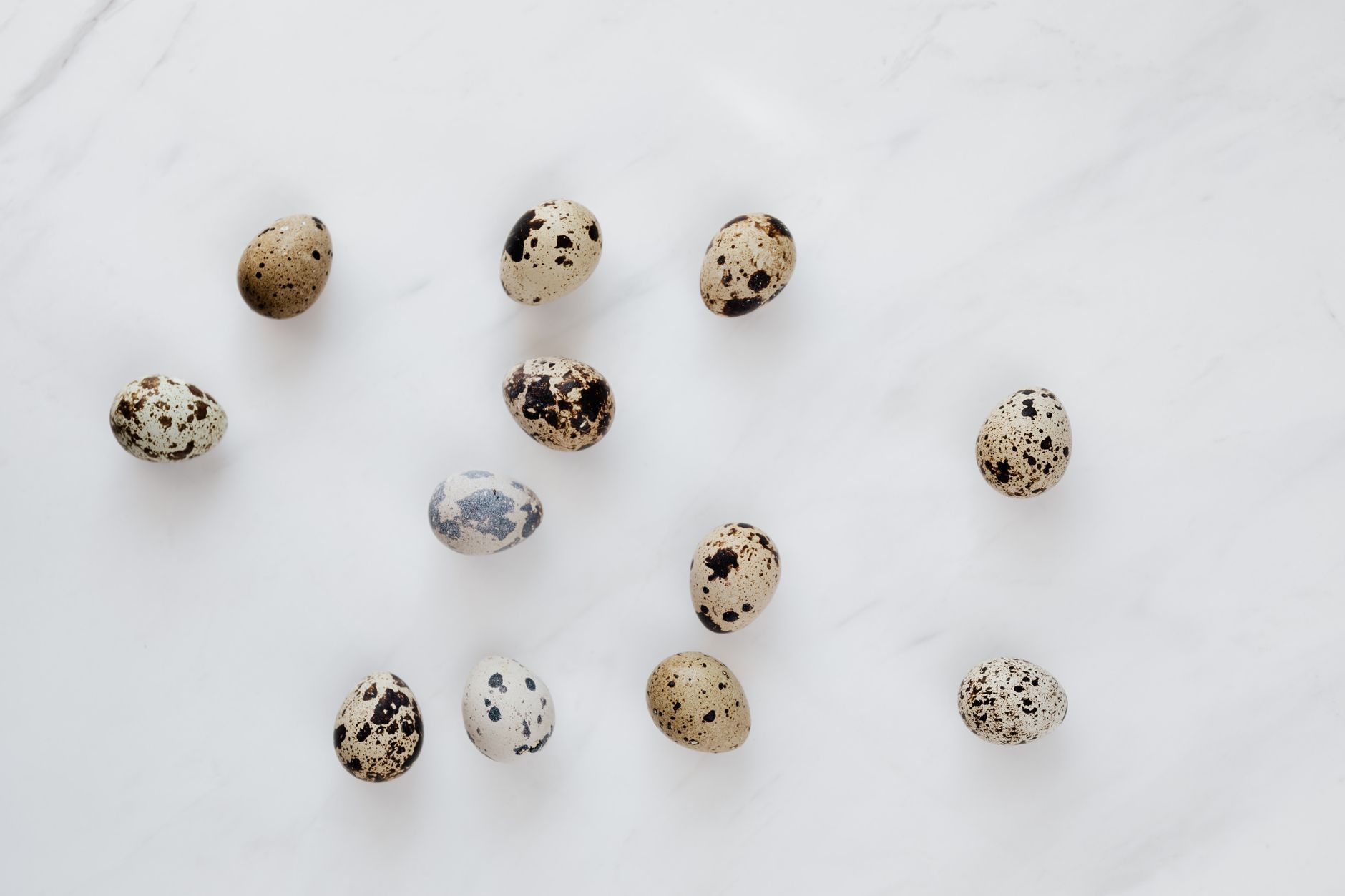 Top view of natural quail eggs placed chaotically on white table during cooking process in kitchen