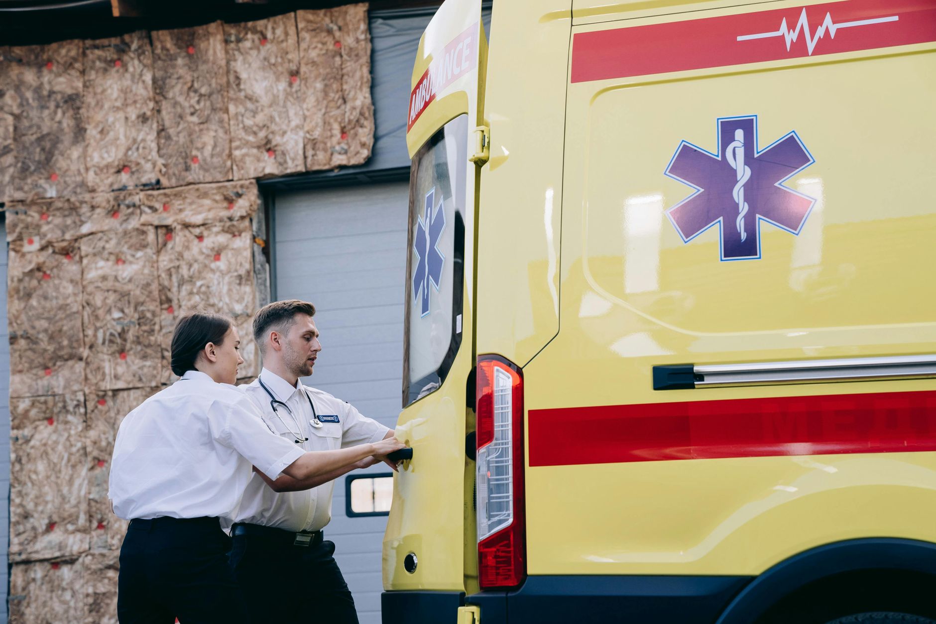 Two paramedics close the rear doors of an ambulance, preparing for emergency response.