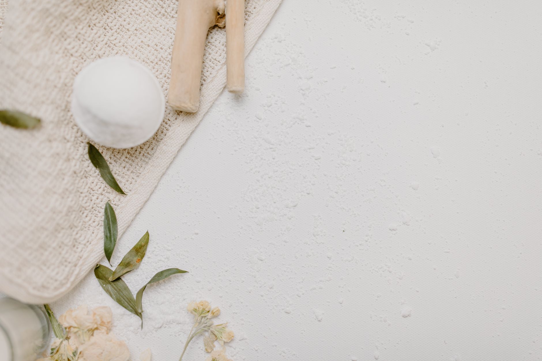 Top view of a spa bath set with a bath bomb, leaves, and flowers on a textured background.
