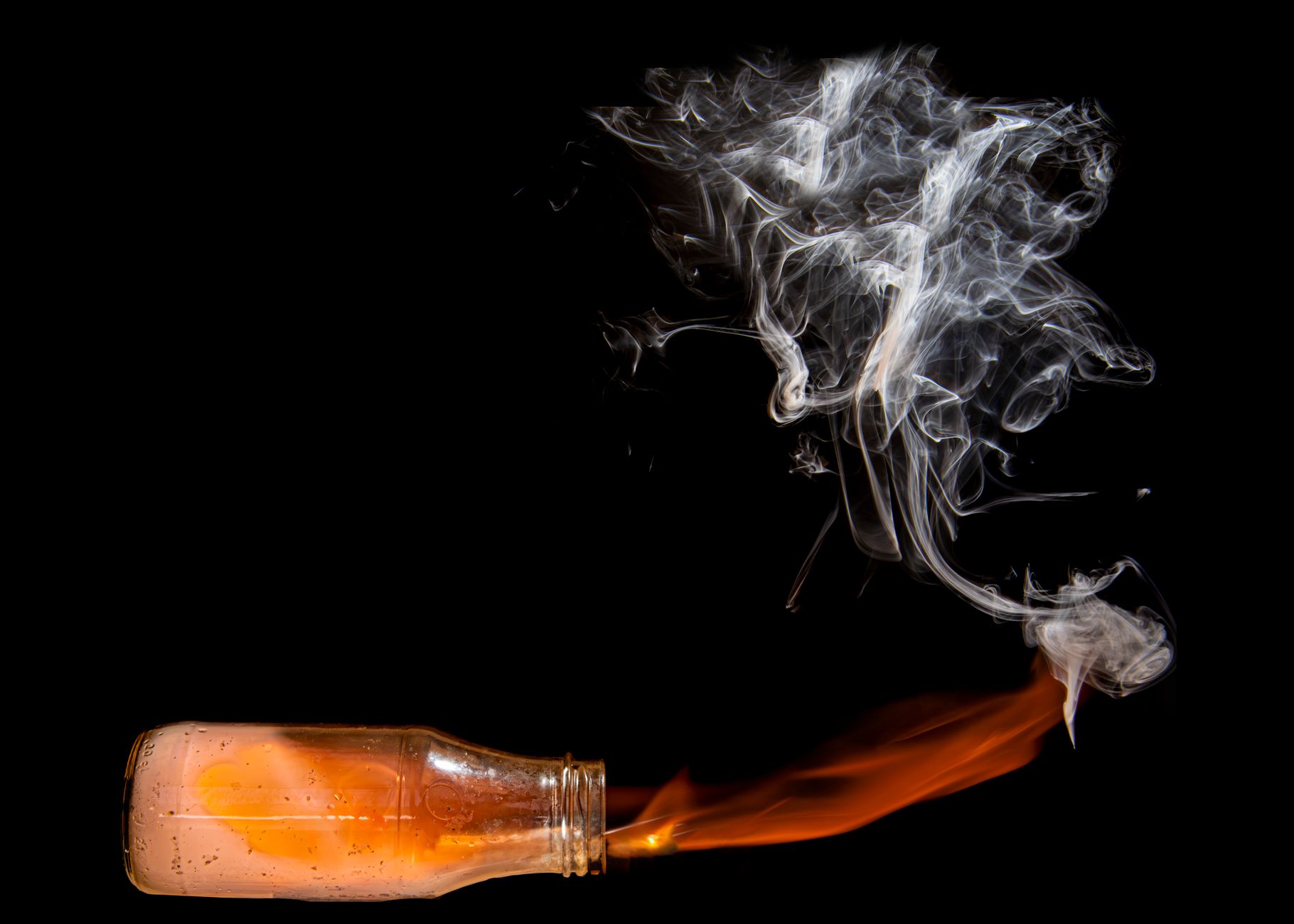 Artistic image of smoke and flame emerging from a glass bottle against a black background.