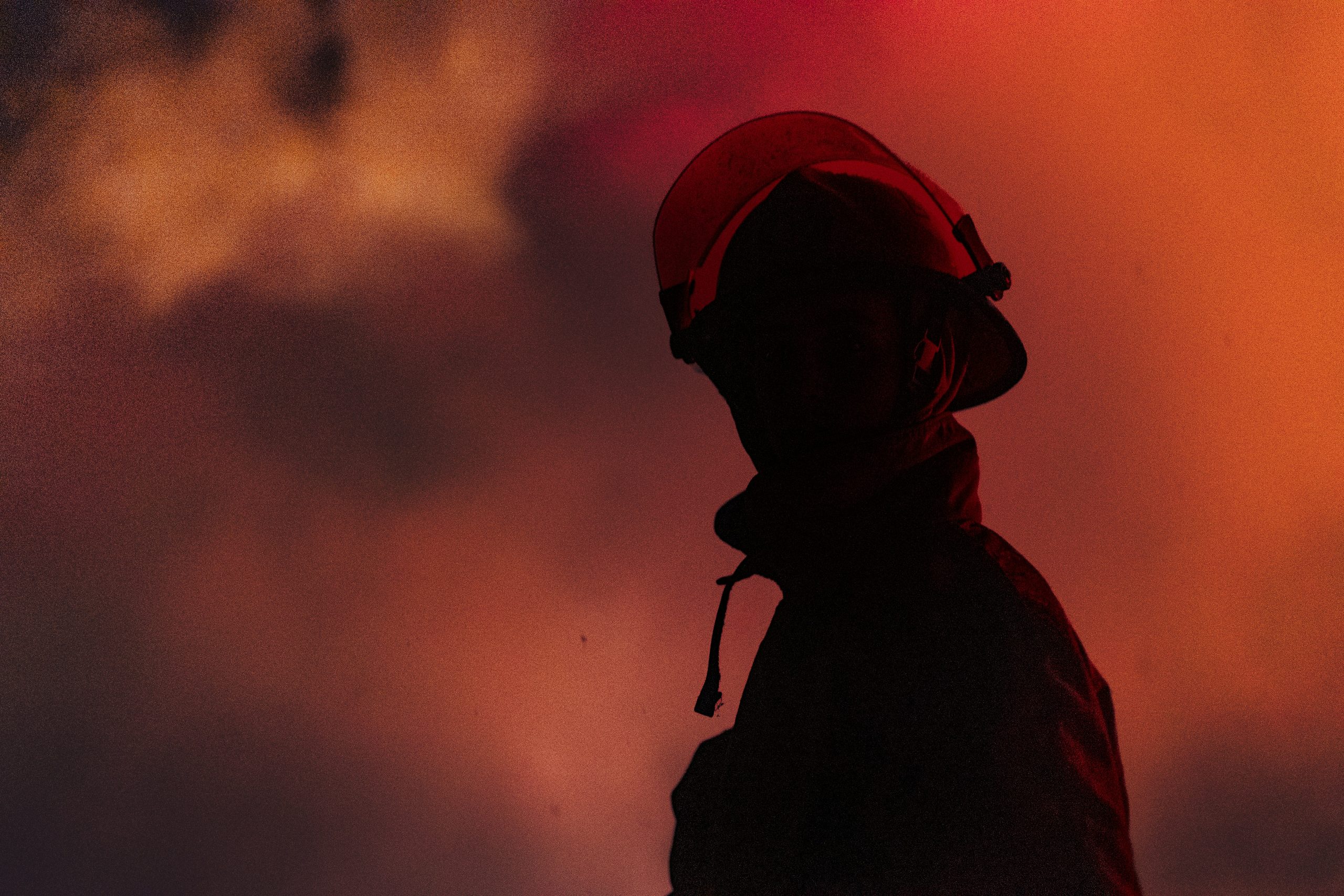A firefighter stands in front of a fiery sky
